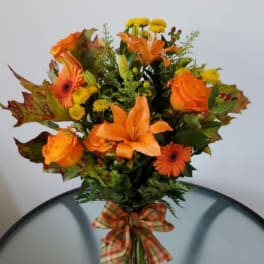 Orange lilies and roses in a glass vase with a plaid bow