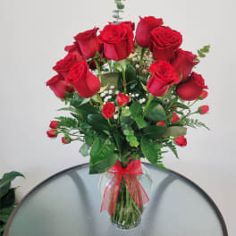 Red roses arranged in a clear glass vase with a red ribbon
