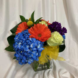 Colorful bouquet with blue hydrangea, orange gerbera daisies, and a yellow ribbon in a glass vase