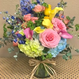 Mixed bouquet with pink roses, yellow calla lilies, and blue flowers in a glass vase