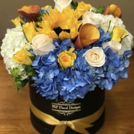 Mixed bouquet of blue hydrangeas, yellow sunflowers, white roses, and orange calla lilies in a black box