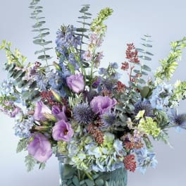 Lavender and blue flowers in a glass vase with tall eucalyptus stems