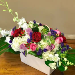Mixed roses and orchids arranged in a white rectangular vase