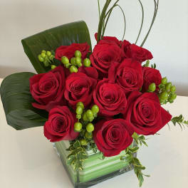 Red roses arranged in a square glass vase with green accents
