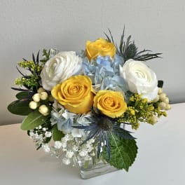 Bouquet of yellow and white roses with blue hydrangeas in a glass vase
