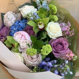 Bouquet of roses, hydrangea, orchids, and green blooms in paper wrap