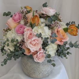 Round arrangement of blush roses, white hydrangeas and pink ranunculus in a textured gray ceramic vase