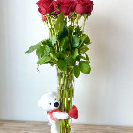Red roses in a tall glass vase with a small teddy bear attached