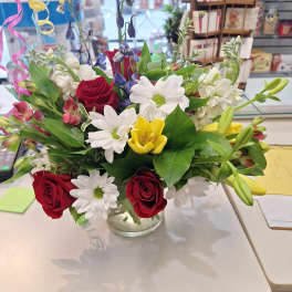 Mixed bouquet of red roses, white daisies, and yellow lilies in a glass vase