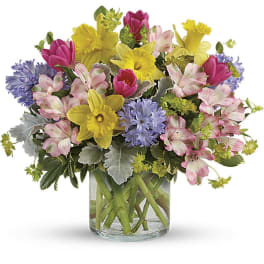 Colorful bouquet of tulips, daffodils, alstroemeria, and blue flowers in a glass vase