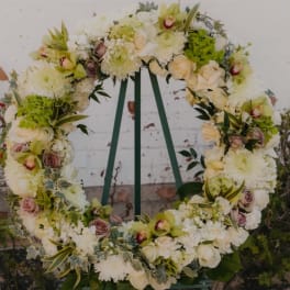 Large floral wreath on a stand with white, cream, and green flowers