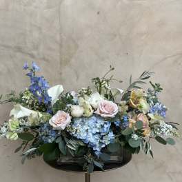Pastel floral arrangement with blue hydrangeas, pink roses, and white calla lilies in a low vase