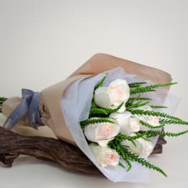 Bouquet of white roses wrapped in brown paper with green filler