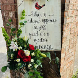 Standing floral easel with red, white, and green flowers beside a memorial sign