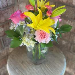 Bouquet of yellow lilies, pink roses, and carnations in a glass vase