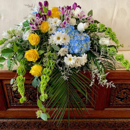 Large floral spray with yellow roses, blue hydrangeas, and white daisies