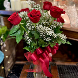 Red roses arranged in a glass vase with white baby's breath and a red ribbon.