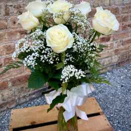 White roses and baby's breath in a clear glass vase with a white ribbon