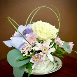 Small pastel flower arrangement in a white cup on a saucer