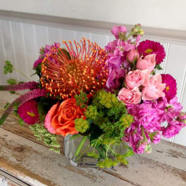 Mixed bouquet of pink, orange, and purple flowers in a clear glass vase