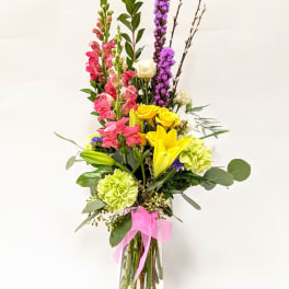Tall mixed bouquet in a clear glass vase with pink, yellow, and purple flowers