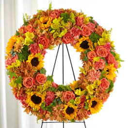 Large floral wreath with roses, sunflowers, and mums on a black stand