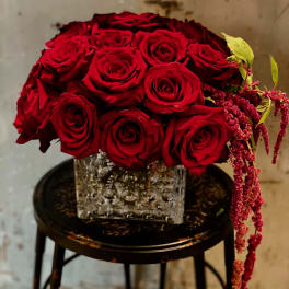 Red rose bouquet in a square glass vase with trailing pink accents