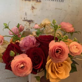 Bouquet of red, pink, and yellow roses with ranunculus in a white vase