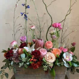 Mixed floral arrangement in a rectangular wooden planter with tall branching stems