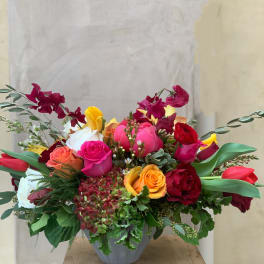 Mixed bouquet of roses, tulips, and orchids in a gray vase