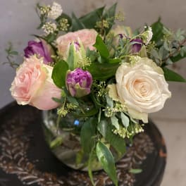 Bouquet of pale pink and cream roses with purple tulips in a glass vase