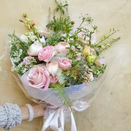 Handheld bouquet of pink and white flowers wrapped in clear paper with a white ribbon