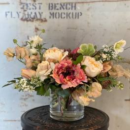 Mixed bouquet of peach, pink, and white flowers in a clear glass vase