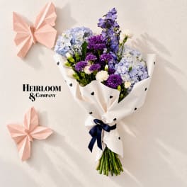 Bouquet of purple, blue, and white flowers wrapped in white paper with black hearts