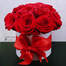 Red roses arranged in a white round box with a red ribbon bow