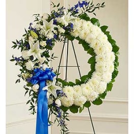 White floral funeral wreath with blue ribbon on an easel