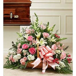 Pink and white floral funeral spray in a wicker basket with a ribbon bow
