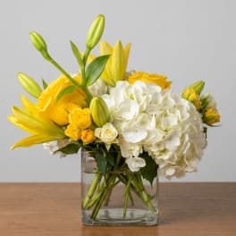Yellow lilies and roses with white hydrangeas in a clear glass vase