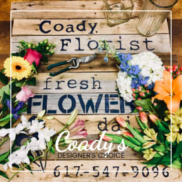 Mixed flower arrangement around a rustic Coady Florist sign