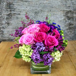 Pink and purple rose arrangement in a square glass vase