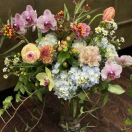 Mixed bouquet with orchids, hydrangeas, and small daisies in a glass vase
