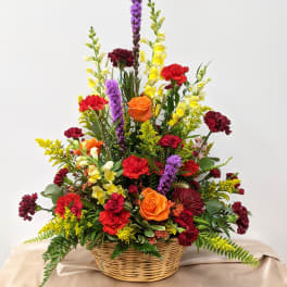 Mixed flower arrangement in a wicker basket with orange roses and red carnations