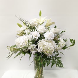 White floral arrangement in a clear glass vase with lilies and roses