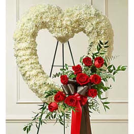 Heart-shaped white floral wreath with red roses on a stand