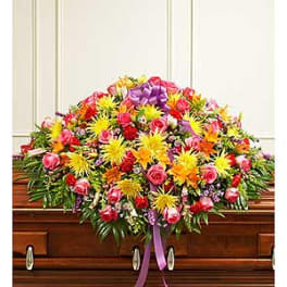 Colorful floral casket spray with roses and daisies on a wooden casket