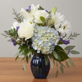 White roses, lilies, daisies, and blue hydrangea in a dark blue vase