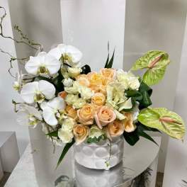 White orchids and peach roses in a white vase with green anthuriums