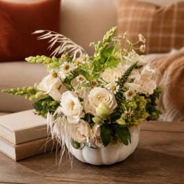 White floral arrangement in a white pumpkin-shaped vase on a table