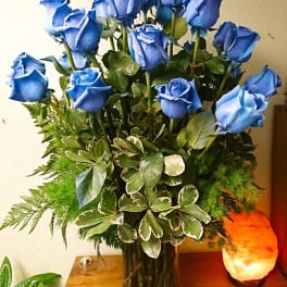 Blue roses arranged in a glass vase with mixed greenery
