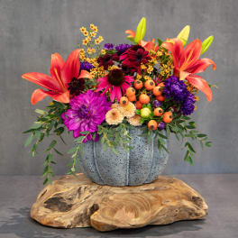 Colorful floral arrangement in a gray pumpkin-shaped vase on a wooden base